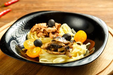 Spaghetti yuvalı siyah tabak bir tezgahta kıçı kırık tavuk filetosu ve mantarla doldurulmuş.