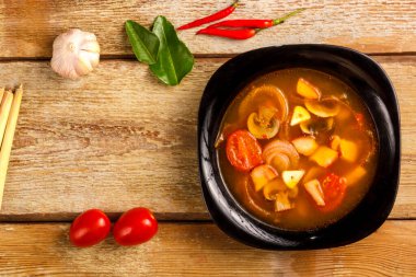 Geleneksel Tayland çorbası Tom Yam ahşap bir masada, sarımsak ve limon otunun yanında, kaffir limonu, kırmızı biber ve kiraz..