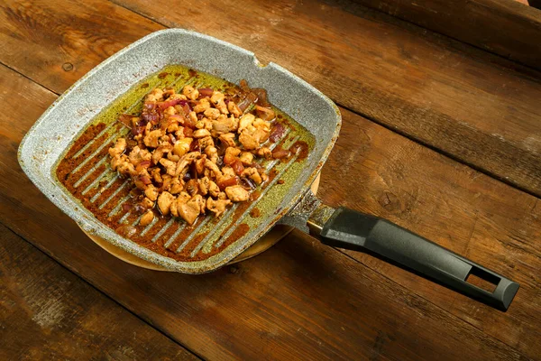 Сковородка с жареным филе курицы и луком на деревянном столе. — стоковое фото