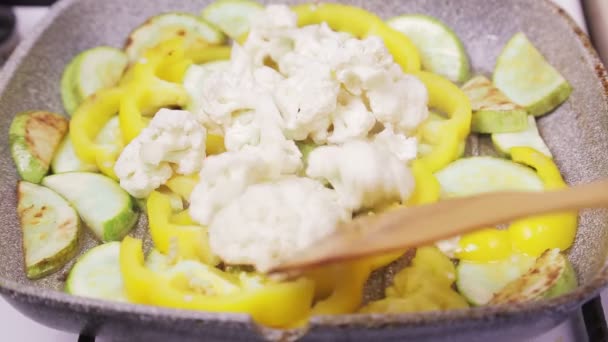 Una mano de mujer con una espátula mezcla verduras en una sartén — Vídeo de stock
