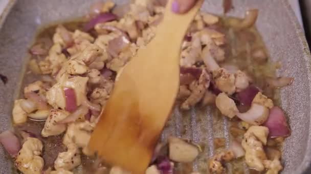 Una spatola mescola il filetto di pollo fritto con la cipolla in una padella. — Video Stock