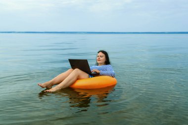 Kadın sabah sularında yüzme çemberinde dizüstü bilgisayarla uzaktan çalışıyor..