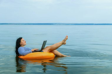 Kadın, suda yüzme çemberinde dizüstü bilgisayarla uzaktan çalışıyor..