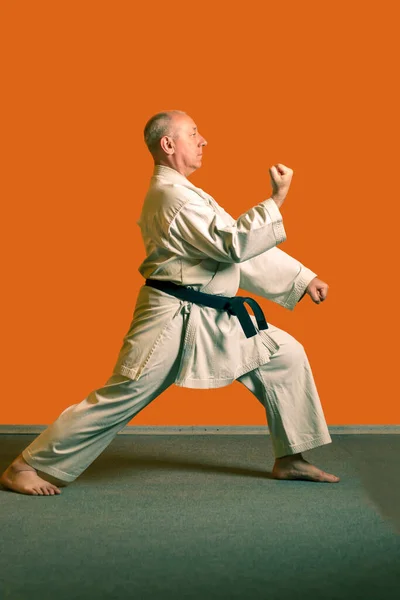 Ein Karate-Mann im weißen Kimono mit schwarzem Gürtel bereitet sich auf den Wettkampf vor. — Stockfoto