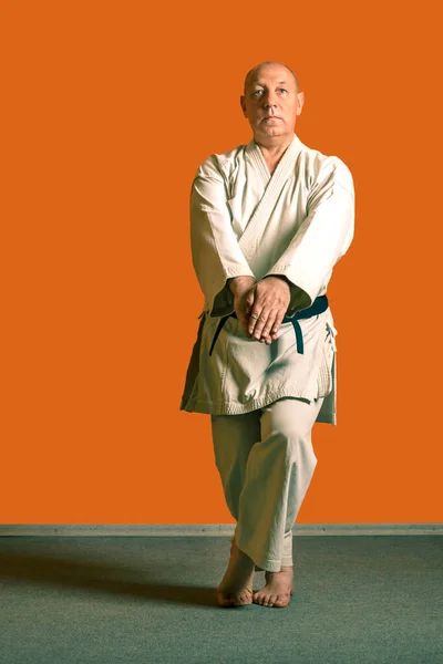 Ein Karate-Mann im weißen Kimono mit schwarzem Gürtel bereitet sich auf den Wettkampf vor. — Stockfoto