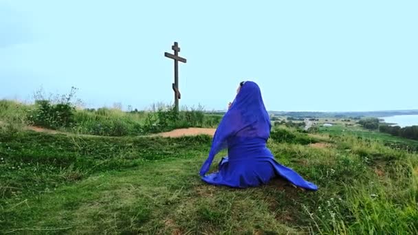 Μια γυναίκα προσκυνήτρια με μπλε και μια κάπα στο κεφάλι προσεύχεται στην κορυφή του βουνού. — Αρχείο Βίντεο