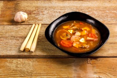 Geleneksel Tayland çorbası Tom Yam, ahşap bir masada, sarımsak ve limon otunun yanında..