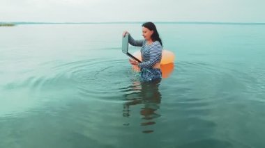 Serbest çalışan bir kadın, denize yakın bir yerden suya düşürdüğü bir dizüstü bilgisayarı alır..