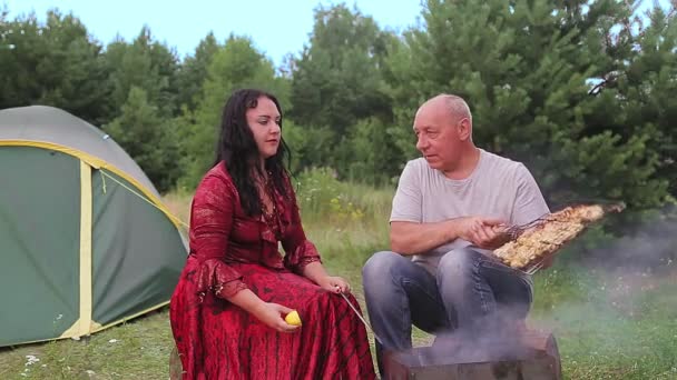 Um casal e uma esposa cigana estão grelhando carne perto da tenda . — Vídeo de Stock