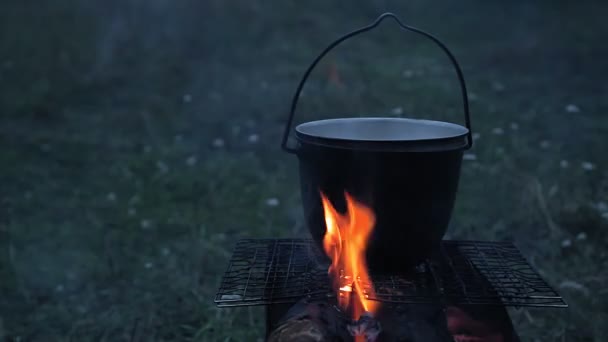 A cauldron with a lid boiling on a fire on a dance at dusk. — Stock Video