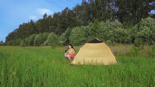 Um quadricóptero com uma função de localização voando sobre uma tenda em que uma mulher está bebendo chá com um livro — Vídeo de Stock