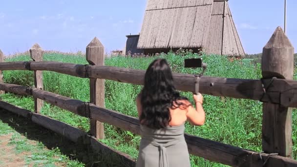 Een vrouw blogger is uitzendingen van de top van een berg praten over een houten tempel. — Stockvideo