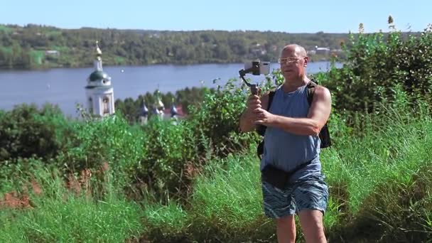 一位男性博主正在山顶上广播，俯瞰河流 — 图库视频影像