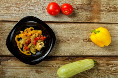 Siyah bir tabakta sebze yahnisi ve ahşap bir masada birkaç sebze..