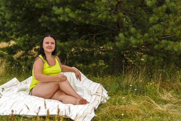 Uma jovem se senta em uma colcha em uma clareira . — Fotografia de Stock