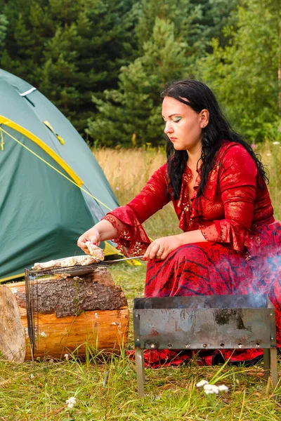 Una joven gitana pone carne en la parrilla junto al fuego . —  Fotos de Stock