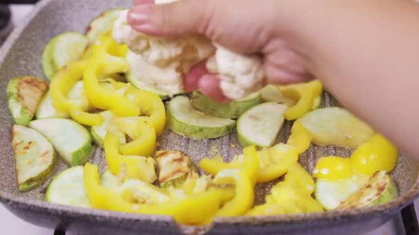 En kvinnlig hand lägger blomkålsskivor i en kastrull med kokande olja och zucchini — Stockvideo