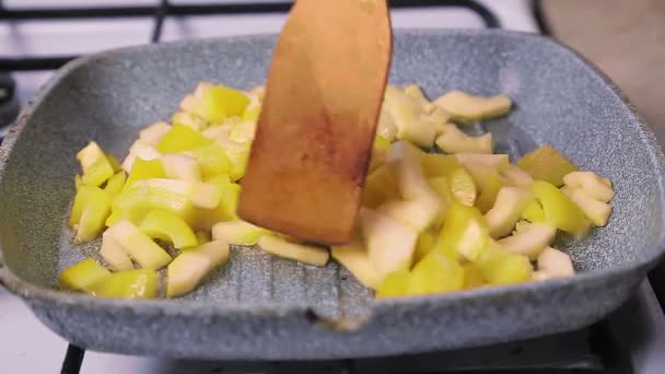 Τα κομμένα κολοκυθάκια με πιπέρι ανακατεύονται σε ένα τηγάνι με ξύλινη σπάτουλα.. — Αρχείο Βίντεο