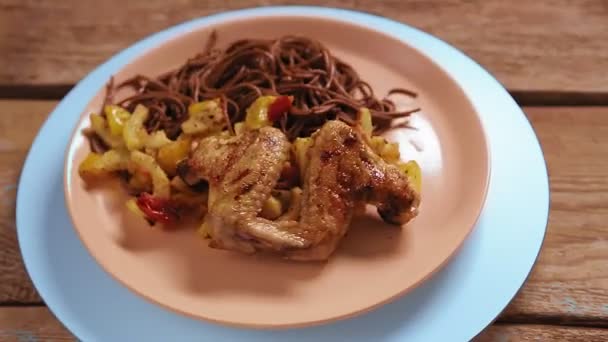 Buckwheat soba noodles with vegetables and chicken wings in a beige plate rotate in a circle. — Stock Video