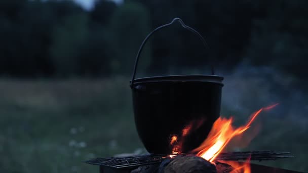 A cauldron with a lid boiling on a fire on a dance at dusk. — Stock Video