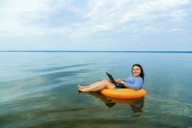 Kadın sabah sularında yüzme çemberinde dizüstü bilgisayarla uzaktan çalışıyor..