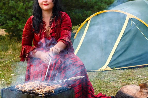 Молодая умная цыганка жарит мясо на гриле возле палатки в дыму от огня.. — стоковое фото
