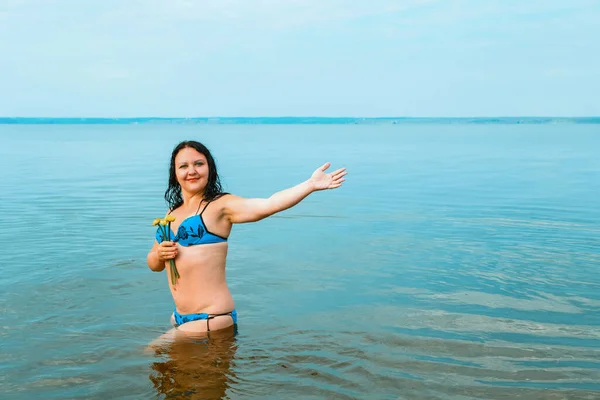 En brunett kvinna i baddräkt i gryningen i det azurblå vattnet nära stranden. — Stockfoto