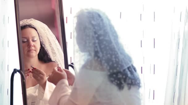 Una novia judía en un vestido y un velo delante de un espejo se aplica maquillaje antes de la ceremonia chuppah. — Vídeos de Stock