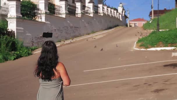 Una bloguera con teléfono móvil habla de viajar por un pequeño casco antiguo. — Vídeo de stock