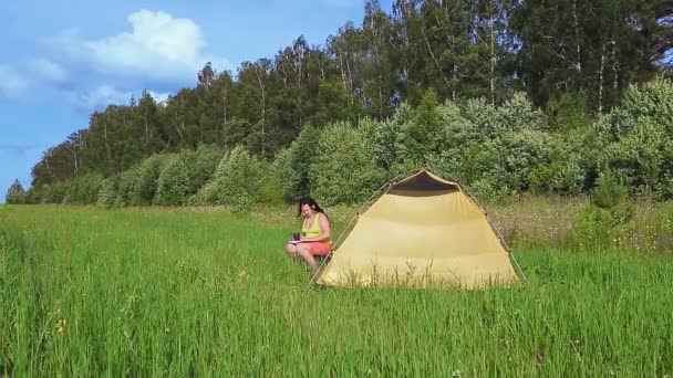 Çadırın yanında bir kadın kitap okuyor ve çay içiyor.. — Stok video