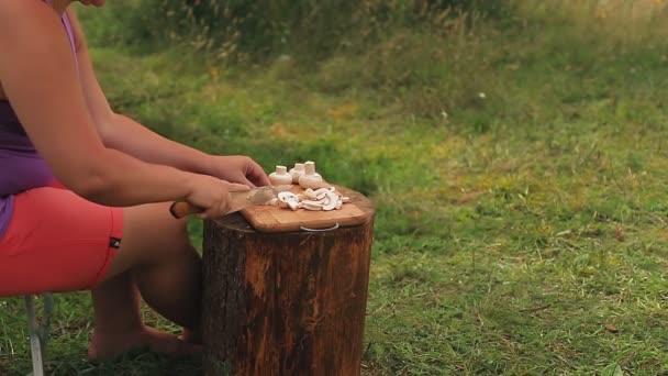 Een vrouw snijdt paddenstoelen met een mes op een houten plank bij een picknick. — Stockvideo