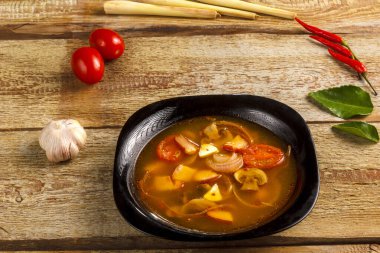 Geleneksel Tayland çorbası Tom Yam, ahşap bir masada, sarımsak ve limon otunun yanında, kaffir limonu, kırmızı biber ve kiraz..