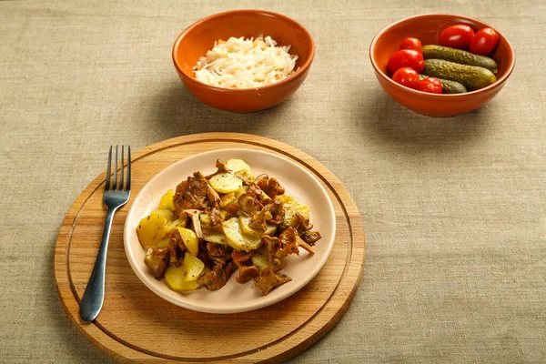 Patatas con larvas de setas en una entrega redonda y un tenedor junto a pepinos en escabeche y tomates y col. —  Fotos de Stock