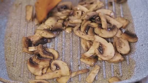 En kvinnlig hand med en spatel blandar de stekta svamparna i en stekpanna — Stockvideo