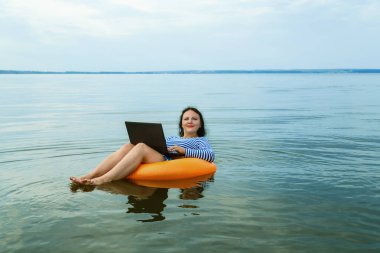 Kadın, suda yüzme çemberinde dizüstü bilgisayarla uzaktan çalışıyor..
