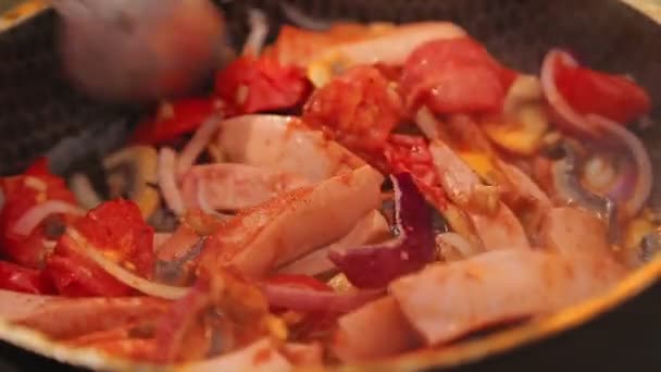 一个女人用勺子把炒鸡蛋、蔬菜和香肠混合在煤块上的煎锅里. — 图库视频影像