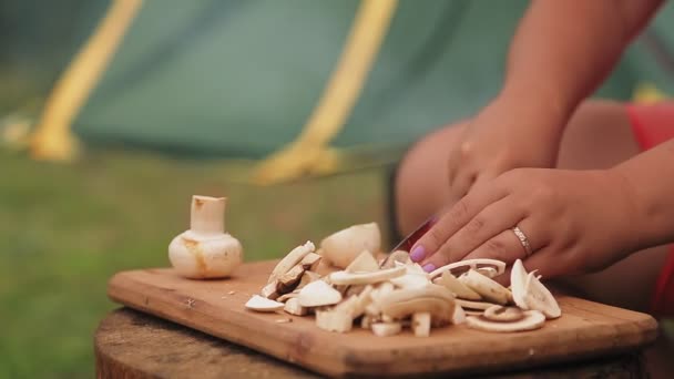 Une femme coupe des champignons avec un couteau sur une planche de bois lors d'un pique-nique — Video