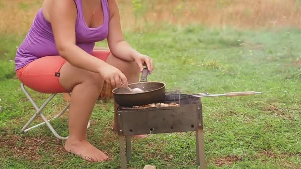 En kvinde blander strimlet pølse med svampe i en stegepande på kullene. – Stock-video