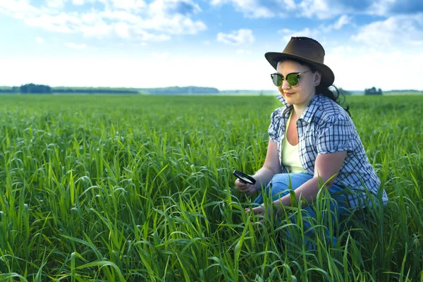 En kvinnlig agronom på fältet undersöker groddarna av grödor i ett förstoringsglas. — Stockfoto