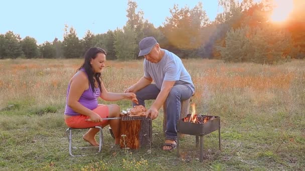 Un hombre y una mujer en la naturaleza preparan carne para asar junto al fuego. — Vídeos de Stock