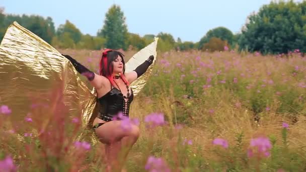 Uma mulher na forma de um demônio em um espartilho preto com asas douradas no campo corre e bate suas asas — Vídeo de Stock