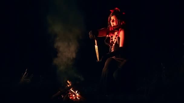 En kvinna i form av en djävul med horn på natten vid elden med kniv dansar en rituell dans i röken. — Stockvideo