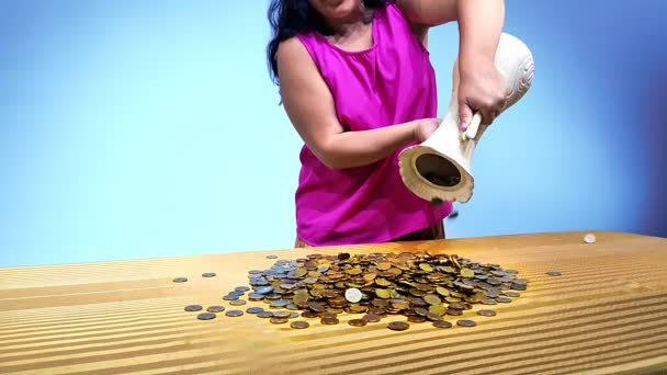 Женщина выливает монеты из большого кувшина на стол. — стоковое видео
