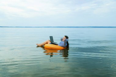 Tatildeki kadın, sabahları yüzme çemberinde dizüstü bilgisayarla uzaktan çalışıyor..