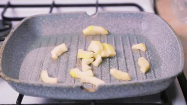 Bir kadının eli, dilimlenmiş kabağı tereyağlı bir tavaya koyar..