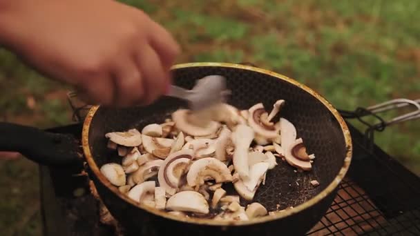 Жінка перемішує смажені гриби з ложкою на сковороді на вугіллі — стокове відео