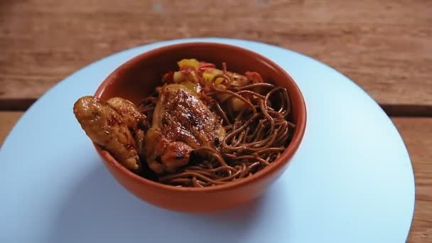 Makaron soba z gryki z warzywami i skrzydełkami kurczaka w beżowym talerzu obracać się w kółko — Wideo stockowe