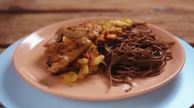 Bej bir tabakta sebzeli karabuğday sobalı erişte ve tavuk kanadı daire şeklinde döner. Ortam planı
