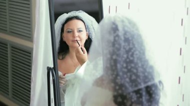 Ayna önünde duvak ve elbise giymiş Yahudi bir gelin aynaya yansıyan hupa töreninden önce makyaj yapar. Ortam planı