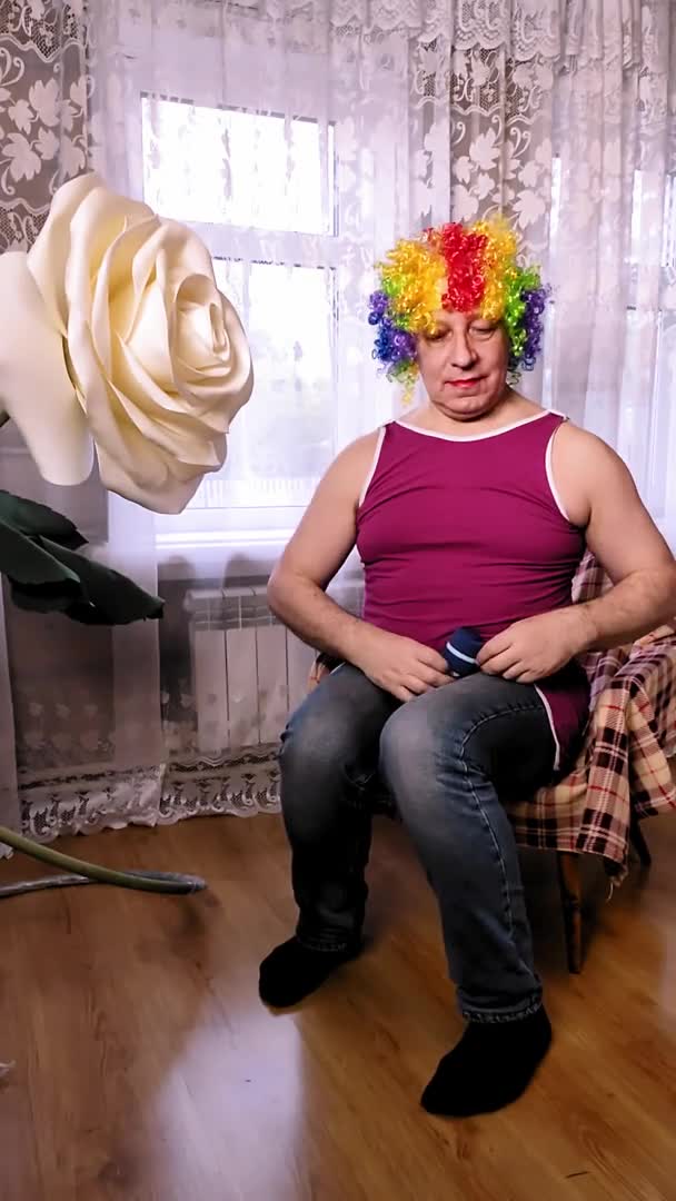 Un homme drôle dans une perruque multicolore avec un travesti maquillage secoue ses biceps avec un haltère. Vertical — Video